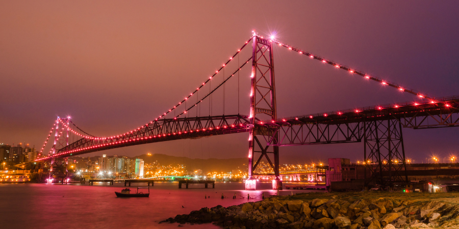 foto noturna da ponte de Florianópolis com luzes rosa em toda ela