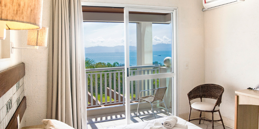 quarto do hotel, cortina, sacada com vista para o mar, cadeira palha, ar condicionado na parede