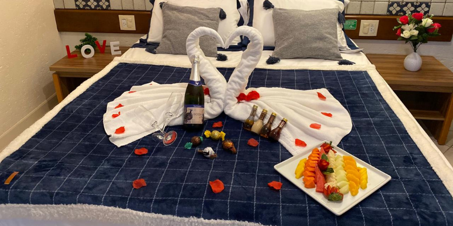 cama com colcha azul, dois cisnes feitos nas toalhas, prato de frio, champagne e duas taças