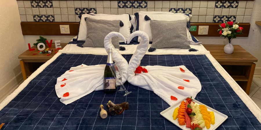 dois cisnes feitos de toalha em cima da cama, prato de frios e espumante em cima da cama