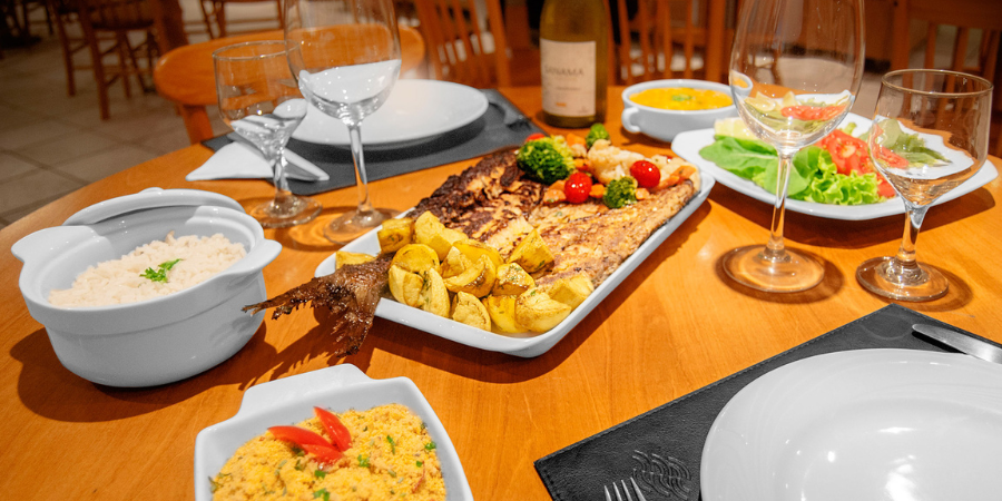 mesa posta com prato de peixe, batata, arroz e farofa