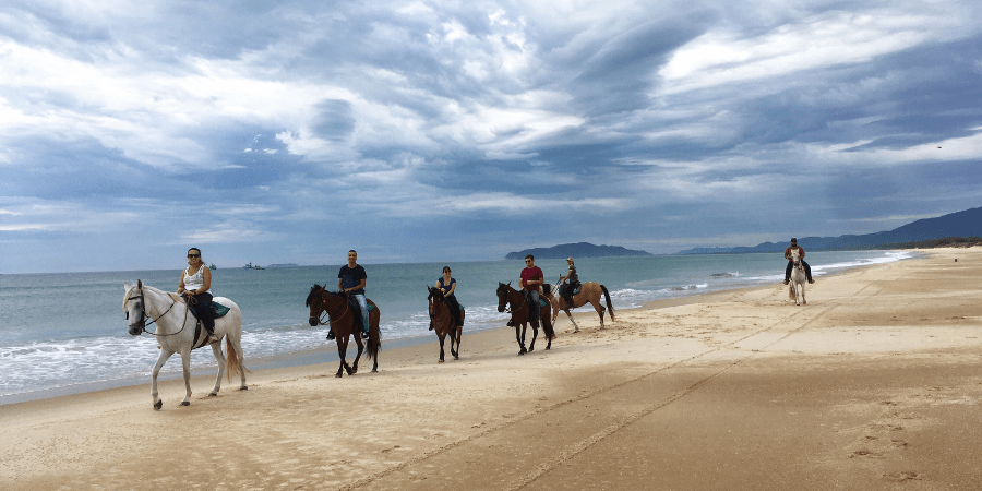 pessoas andando a cavalo na beira da praia