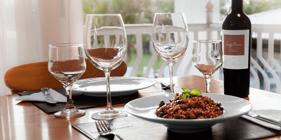 mesa posta com prato de risoto, taças e garrafa de vinho